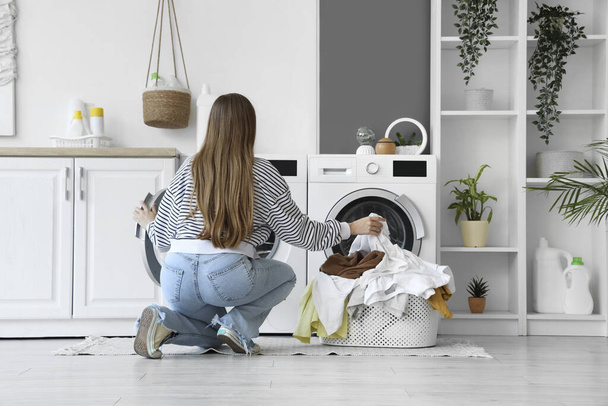 Jovem mulher colocando roupas sujas na máquina de lavar roupa na lavanderia, vista traseira - Foto, Imagem
