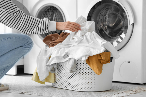 Çamaşır odasındaki çamaşır makinesine kirli çamaşırları koyan genç bir kadın. - Fotoğraf, Görsel