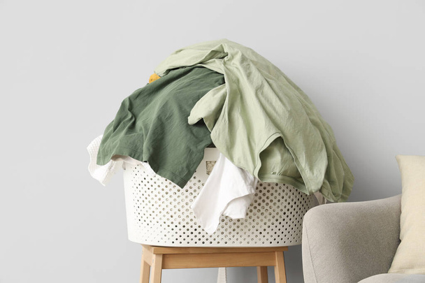 Korb mit schmutziger Wäsche auf Hocker nahe Lichtwand - Foto, Bild