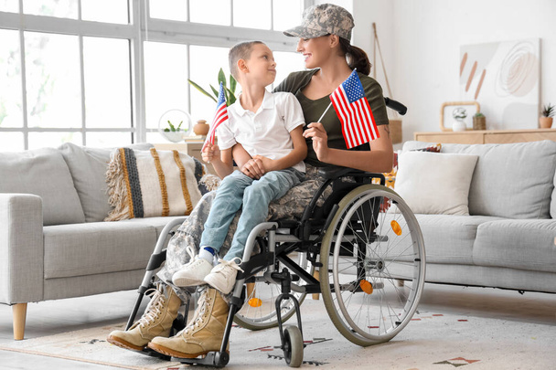 Soldato donna e il suo piccolo figlio con bandiere USA in sedia a rotelle a casa - Foto, immagini