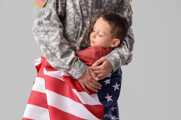 Женщина-солдат обнимает своего маленького сына с флагом на светлом фоне. Празднование Дня ветеранов - Фото, изображение