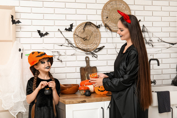 Madre dando a su pequeña hija dulces de Halloween en la cocina - Foto, Imagen