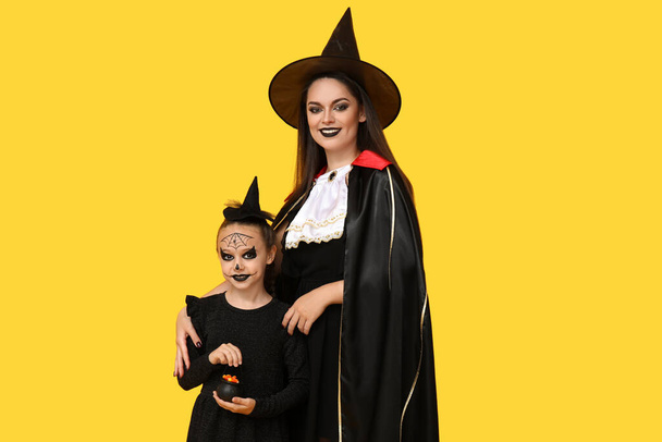 Annesiyle Cadılar Bayramı için sarı arka planda giyinmiş küçük bir kız. - Fotoğraf, Görsel