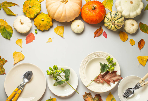 Thanksgiving festive table composition with different colourful pumpkins, autumn leaves, empty plates with cutlery on light grey background table ready for party and celebration. Space for text.. - Photo, Image