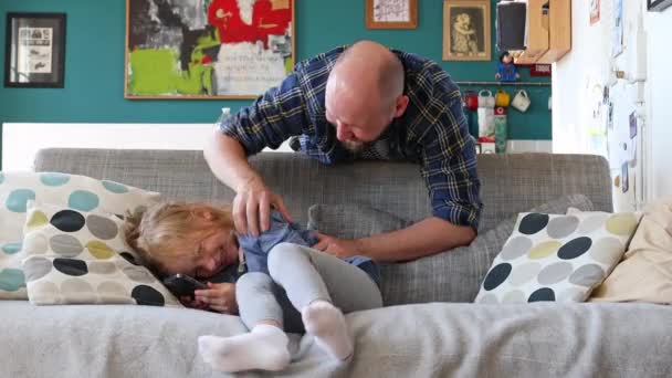 Папа щекочет дочь на диване дома - Кадры, видео