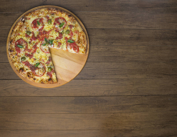 Zdjęcie Pizza Marguerita wykonane z sera Mozzarella, pomidory, liście bazylii i zielone oliwki, serwowane na drewnianej desce. Zdjęcie gastronomiczne Topo w pozycji poziomej. - Zdjęcie, obraz