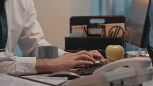 Junge müde männliche Büroangestellte trinkt Kaffee und gähnt, während sie spät in der Nacht am Computer arbeitet - Filmmaterial, Video