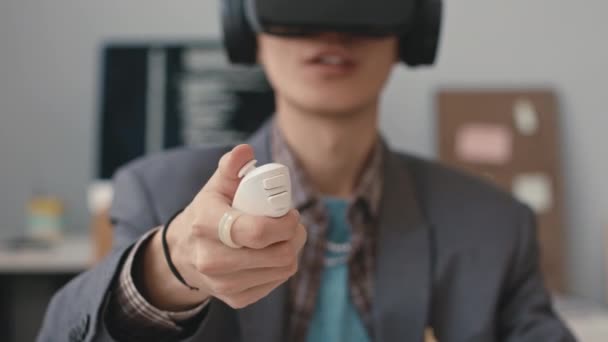 Zbliżenie młodego azjatyckiego inżyniera oprogramowania naciskającego przycisk na kontrolerze podczas doświadczenia z wirtualną rzeczywistością w biurze - Materiał filmowy, wideo