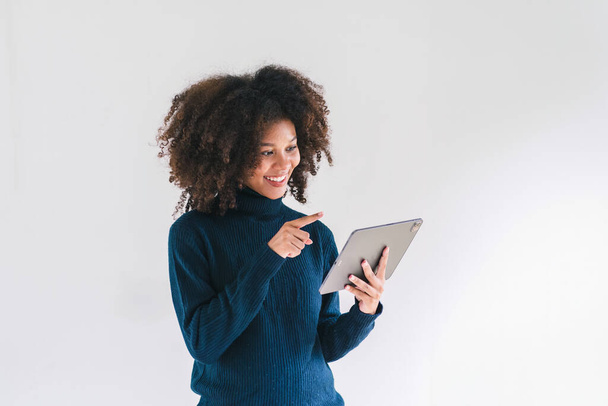 Веселая молодая афро-американская красотка, предприниматель в повседневной одежде, улыбающийся, пользующийся планшетом в современном офисе - Фото, изображение