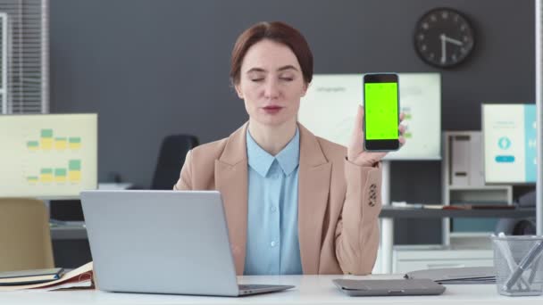 Потерпіти POV молодої кавказької бізнес-леді, демонструючи порожній екран смартфона, сидячи за столом в офісі і виступаючи на камеру - Кадри, відео