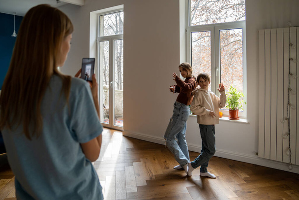 Familie van drie moeder en twee kinderen maken social media content video op smartphone, moderne jonge moeder opnemen van kinderen bloggers dansen voor de telefoon thuis. Bloggen en kleine kinderen - Foto, afbeelding