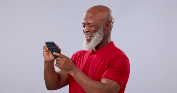 Телефон, посмішка і додаток з старшим чорним чоловіком в студії на сірому фоні для спілкування. Контакт, соціальні медіа та літня людина сміються у коміксі, смішному мемі чи дописі на мобільному телефоні. - Кадри, відео