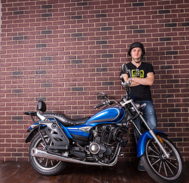 Young Man Standing Beside Motorcycle Against Wall - Foto, Imagen