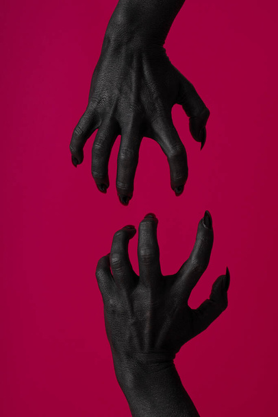 ピンクの背景に黒い爪を持つ黒い女性の手 - 写真・画像