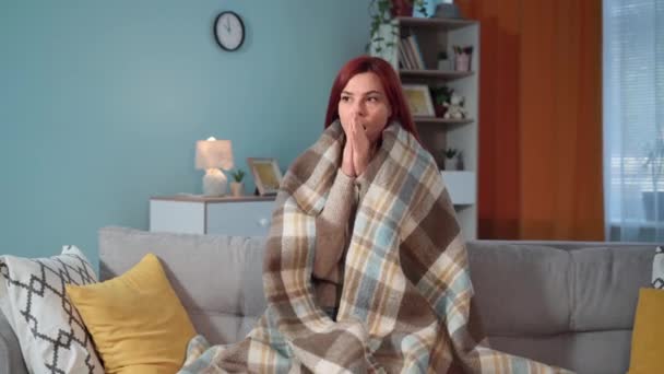nainen lämpimässä huopa istuu sohvalla huoneessa ja yrittää pitää lämpimänä, koska puute lämmitys kotona tai velat apuohjelmia - Materiaali, video