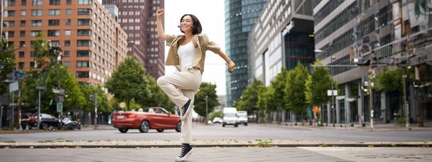Retrato de chica feliz asiática saltando y bailando en el centro de la ciudad, posando en las calles, expresan alegría y emoción. Copiar espacio - Foto, Imagen