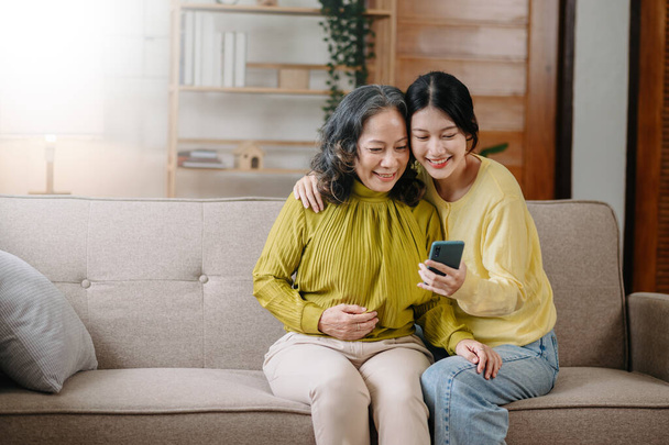 Happy adult granddaughter and senior grandmother having fun enjoying talk sit on sofa in living roo - 写真・画像