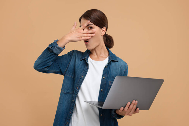 Embarrassed woman with laptop covering face on beige background - Foto, imagen