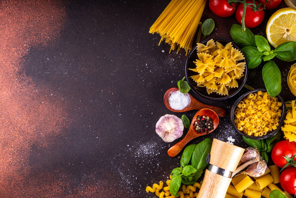 Verschiedene Nudeln mit Gewürzen und Zutaten zum Kochen. Zubereitungsessen, Mittagessen mit frischem Basilikum, Tomaten, Gewürzen, Knoblauch und verschiedenen Arten italienischer mediterraner Pasta - Foto, Bild