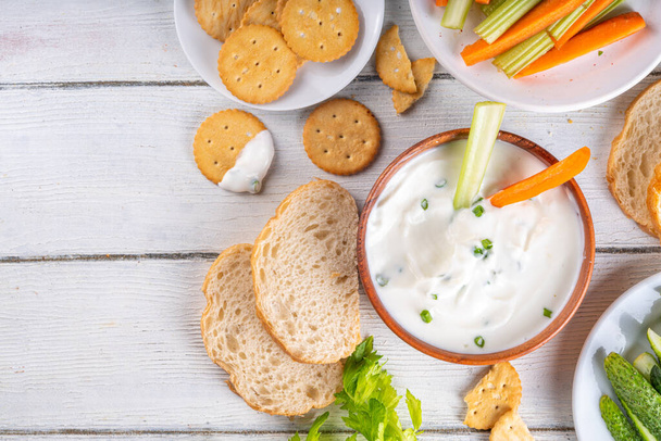 Hüttenkäse-Dip mit hohem Eiweißanteil mit frischem Gemüse, Brot und Crackern auf einem hölzernen weißen Tisch. Ernährung gesunder Quarkaufstrich mit verschiedenen Snacks - Foto, Bild