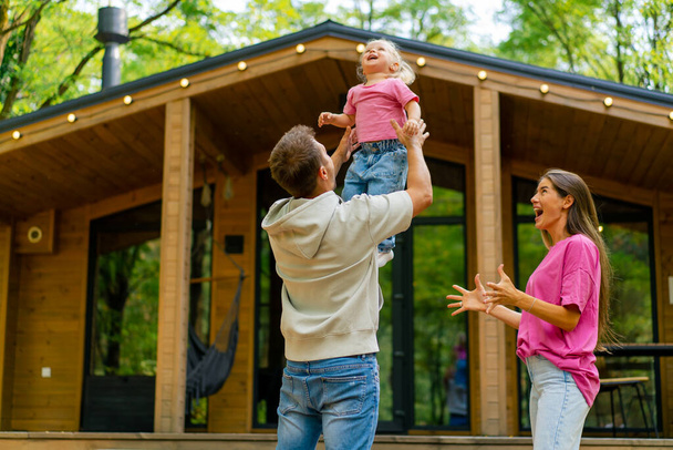 a young family of a man and a woman rejoicing over the purchase of their own wooden house in the forest - Photo, Image