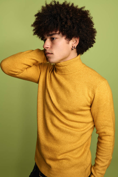Young mixed race model male with Afro hairstyle in yellow sweater standing against green background - Foto, immagini