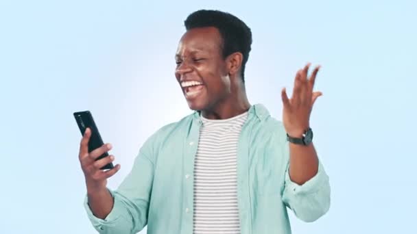 Чорний чоловік, смартфон і підбадьорює кулаком насос і виграє соціальні медіа, ізольовані на синьому фоні. Щастя, захоплення та святкування з онлайн-конкурсом, нагородами та бонусами в студії. - Кадри, відео