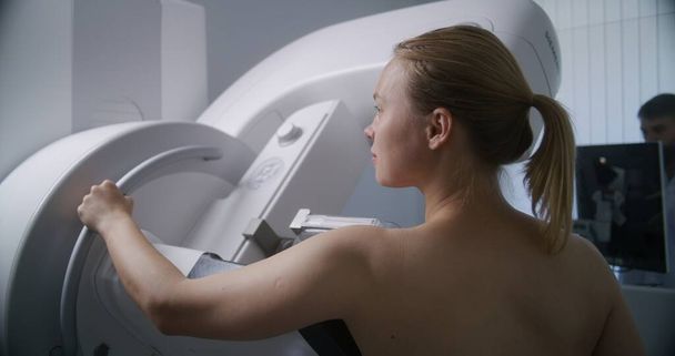 Donna adulta si trova in topless sottoposti a mammografia scansione check-up in sala di radiologia clinica. Il medico maschio installa la macchina della mammografia usando il calcolatore. Prevenzione del cancro al seno. Moderno ospedale luminoso. - Foto, immagini