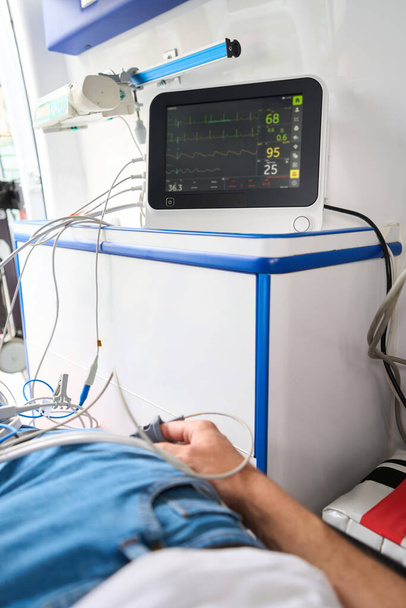 Férfi alkalmi ruhák csatlakozik a kardiográfia egy mentőben, a betegek indikátorai láthatók a monitoron - Fotó, kép