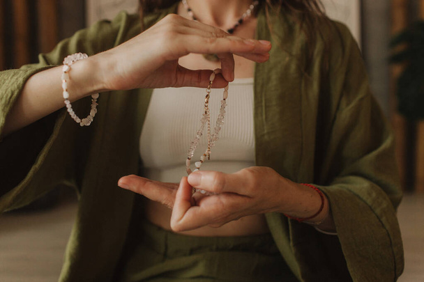 Woman holds jewelry made of natural stones in her hand, her hands are decorated with rings and bracelets. Handicrafts and creativity. Spirituality, religion, God concept. - Photo, Image