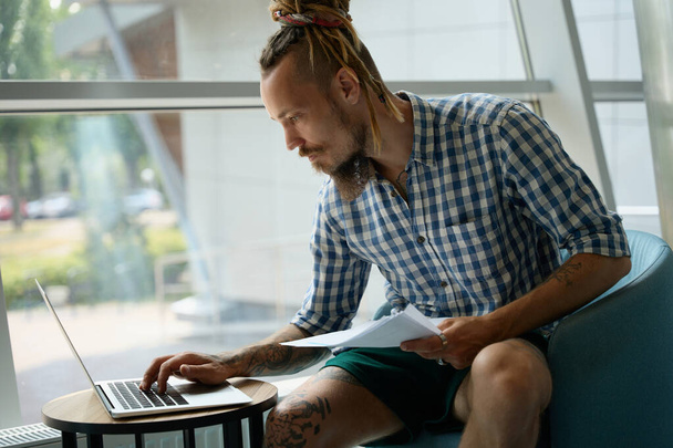 Kerel in een geruit shirt werkt op een laptop in de co-working area, hij is gelegen aan de viewport - Foto, afbeelding