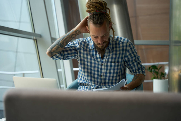 Freelancer in een geruit shirt werkt op een laptop in het coworking gebied, hij is gelegen aan de viewport - Foto, afbeelding