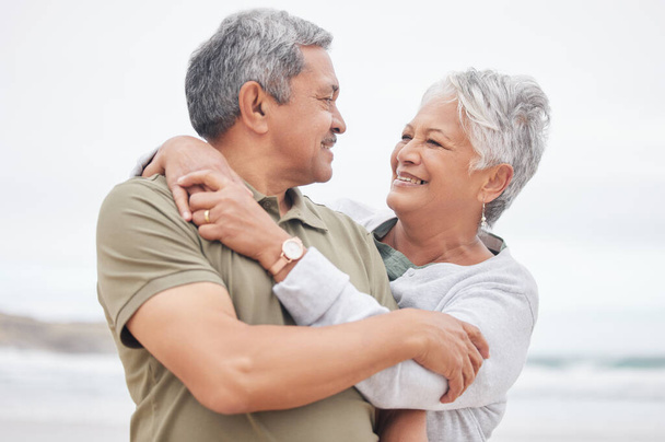 Senior couple, love and hug at beach for holiday, vacation or freedom to travel in retirement together. Happy man, elderly woman and embrace at ocean for trust, loyalty or relax with marriage partner. - Photo, Image