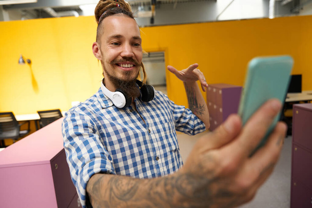 Mies ruudullisessa paidassa ottaa selfien toimistotilassa, tyylikäs sisustus coworking-tilassa - Valokuva, kuva