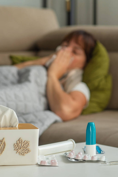 Beteg középkorú nő tüsszentés fújás orrfolyás tartó szövet ülni az ágyon, ideges érett hölgy megfázott kapott influenza grippe tünetek szedése gyógyszerek otthon egyedül - Fotó, kép