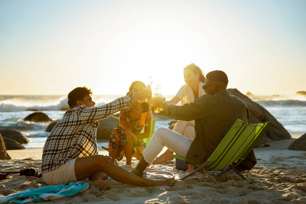 4 φίλοι κάνουν πρόποση στην παραλία το ηλιοβασίλεμα. Υψηλής ποιότητας φωτογραφία - Φωτογραφία, εικόνα