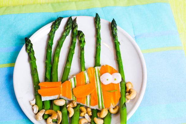 asperges, wortelen, kaas en cashewnoten in de vorm van een broodje vis voor kinderen - Foto, afbeelding