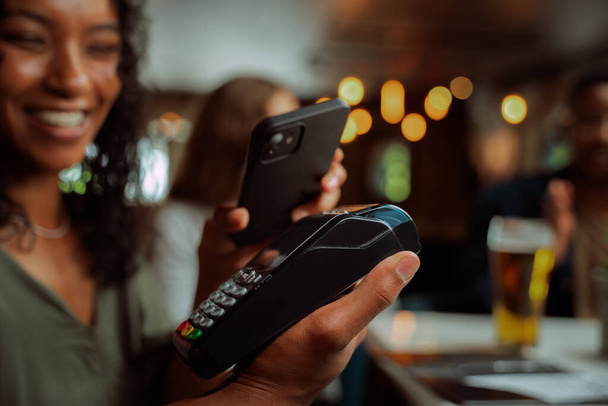 Afro-Amerikan kadın kart makinesinin cep telefonuyla yemek parası ödeniyor. Yüksek kalite fotoğraf - Fotoğraf, Görsel