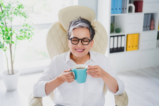 Daylight office view photo of pensioner woman successful business lady enjoy smell aroma morning espresso isolated indoors background. - Fotografie, Obrázek
