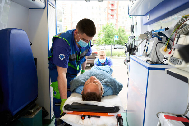 Üniformalı sağlık görevlileri, ambulanstaki bir hastayla birlikte sedyeyi boşaltıyor. - Fotoğraf, Görsel