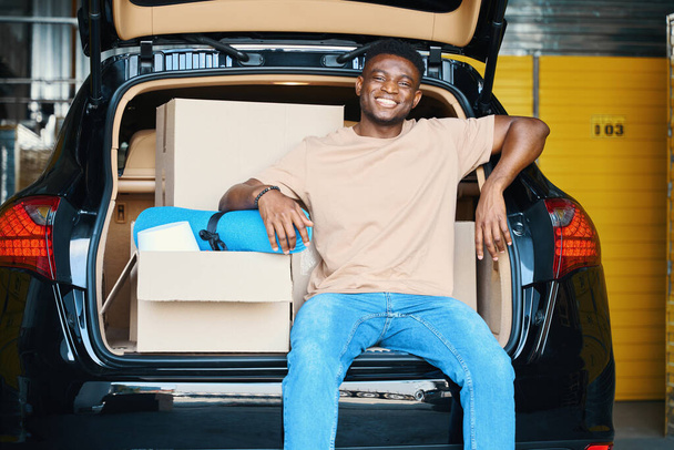 El joven afroamericano está descansando en el maletero de un auto, trajo cosas para almacenarlas al servicio - Foto, imagen