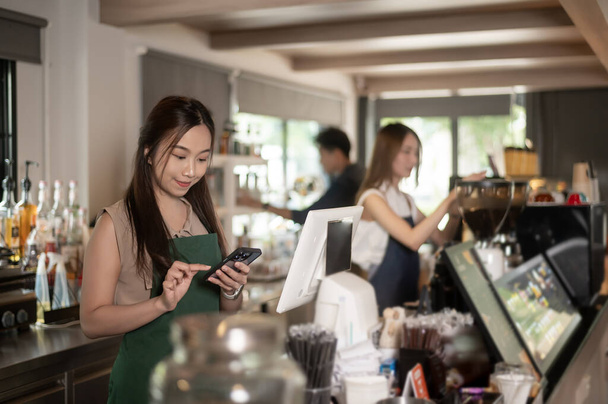 Young Asian service minded barista  with customer in coffee shop - Photo, image