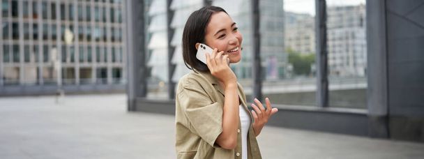 Soluyhteys. Nuori aasialainen nainen tekee puhelun, puhuu mobiili älypuhelin ja kävely kadulla. - Valokuva, kuva