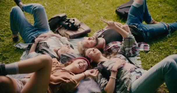 Feliz macho y hembra amigos acostados y disfrutando durante el picnic en el parque - Imágenes, Vídeo