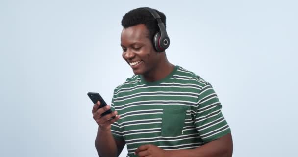 Music, cellphone and happy black man dancing, listening and streaming radio sound, hip hop or rap song. Headphones, media phone app and studio dancer singing, freedom and energy on blue background. - Footage, Video