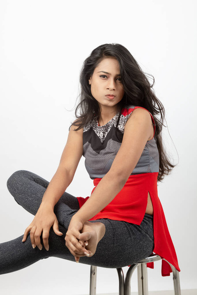Studio girato da una giovane e bellissima modella indiana vestita in modo casual con top di design rosso e grigio e jeans neri su sfondo bianco. Modello femminile. Ritratto di moda. - Foto, immagini