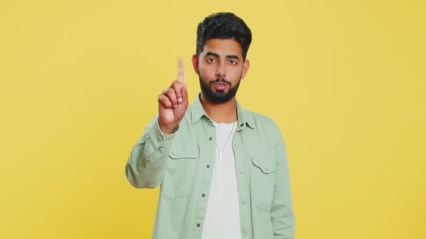 Indian young man shakes finger and saying no, be careful, scolding and giving advice to avoid danger mistake, disapproval sign, disagree, dislike. Arabian guy isolated on yellow studio background - Footage, Video