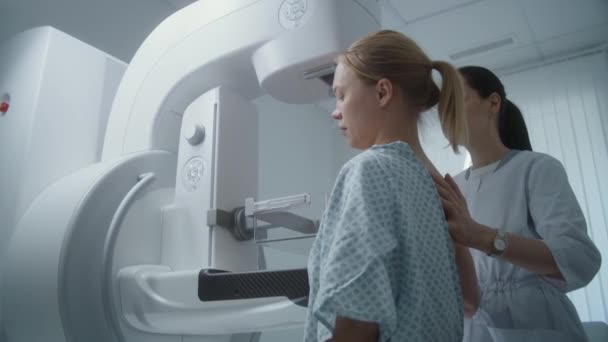 Sala di radiologia dell'ospedale. La donna caucasica è in piedi durante la procedura di screening mammografico. Il dottore femminile aggiusta il mammograph digitale per paziente, usa il computer. Prevenzione del cancro al seno. Clinica moderna. - Filmati, video