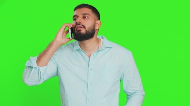 Disinterested Indian man having annoyed boring talk on smartphone. Arabian guy tired sleepy freelancer talking on mobile phone with friend, making online conversation on green chroma key background - Footage, Video