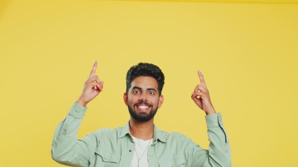 Ινδός γενειοφόρος άνδρας δείχνει αντίχειρες και δείχνει από πάνω, πάνω από το κεφάλι κενό μέρος, διαφημιστική περιοχή για εμπορικό κείμενο αντίγραφο χώρο για την προώθηση των προϊόντων διαφήμιση. Τύπος απομονωμένος σε κίτρινο φόντο - Πλάνα, βίντεο